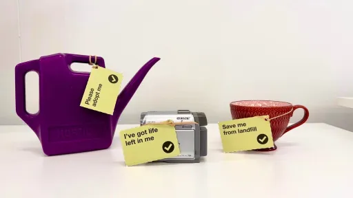 A purple watering can, a camcorder and a red cup with tags encouraging people to save the items from landfill.