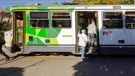 Two people climb into a green and white tram