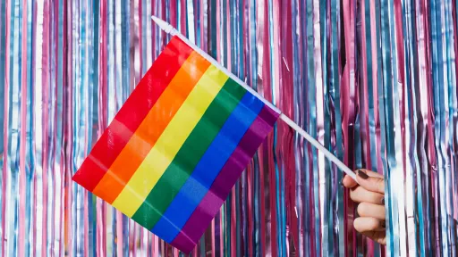 a hand holding a rainbow flag in front of a sparkling curtain