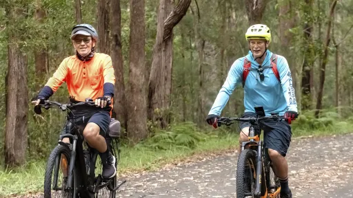 Two men riding bikes on a bike track lined with trees.