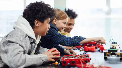 Three children are building lego robots while sitting at a table