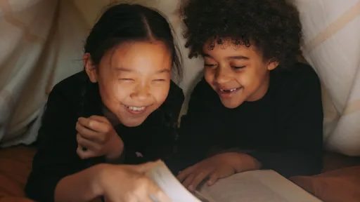 Two children reading a book under a blanket fort