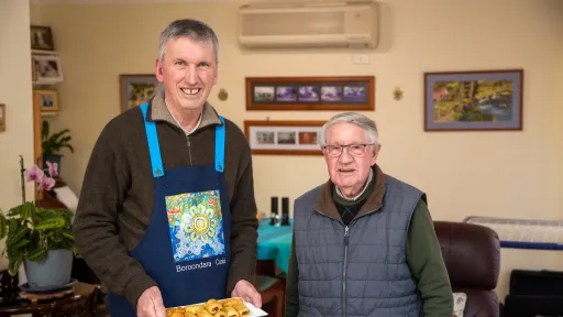 A volunteer holding a plate of food stands with their older neighbour.