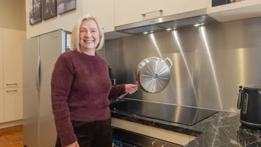Woman in fluffy purple jumper holds shiny pan above black cooktop