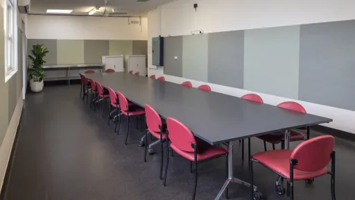 A meeting room with a long desk surounded by red chairs. 