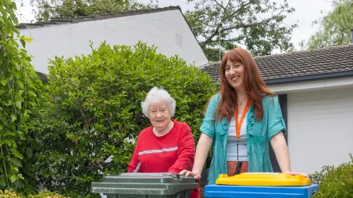 Two people standing behind a general waste and a recycling bin.