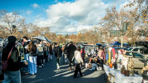 A sunny market day with busy stall and people walking around.