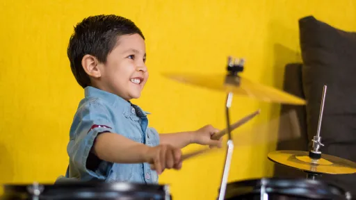 Young child playing drums sitting in front of a yellow background