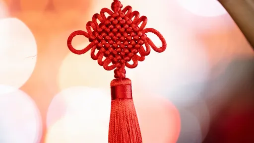 A red chinese knot decoration is being held up by a hand