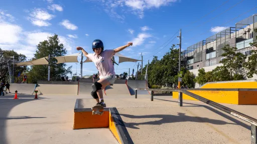 A person wearing helmet and knee pads skates off a ramp in a skate bowl