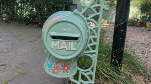A round cast iron letterbox painted in pale green and painted with pink flowers.