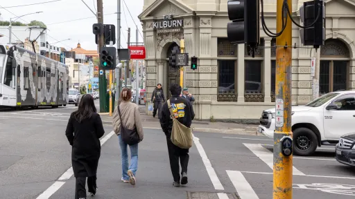 Several people cross a road at traffic lights with pub in background