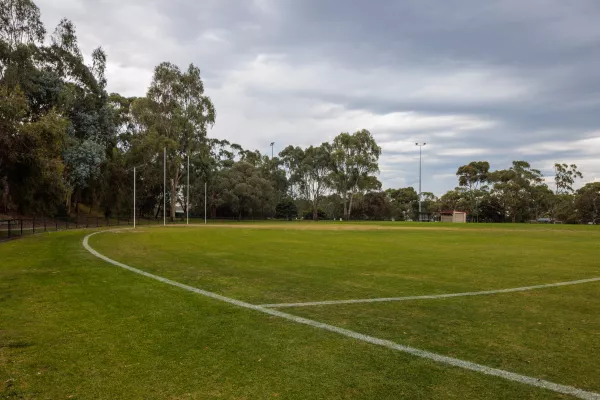 A fenced sports field, with line markings, AFL goal posts and green grass. 