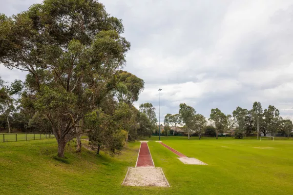 2 red atheletics tracks both with sand pits at the end. Tall trees are to the left, and a sportsground is to the right of the tracks
