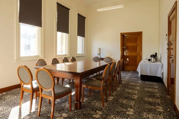 A meeting room with a large table with 12 chairs. A table with a kettle and cups is in the back corner. 