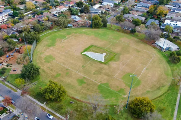 An aerial view of a oval sportsground. It is surrounded by a playground and houses.