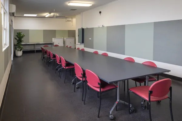 A meeting room with a long desk surounded by red chairs. 