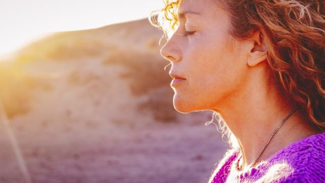 A close up of a person standing on a beach with their eyes closed
