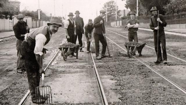 Historical black and white photo of workers with wheelbarrows and pitchforks repairing Riversdale Road