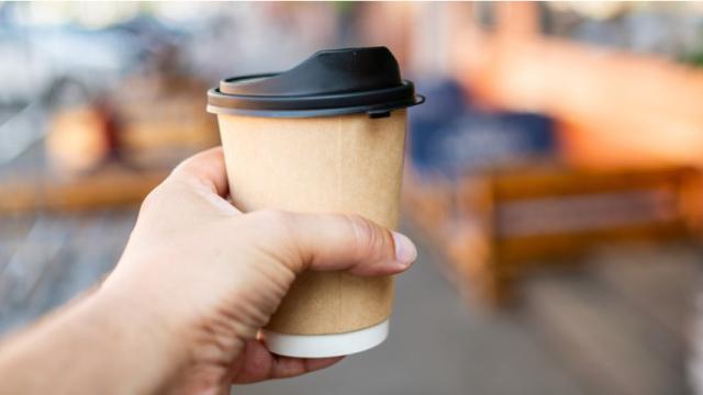 Person's hand holds disposable paper coffee cup with plastic lid