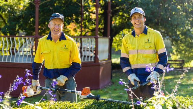 2 people in hi-vis holding whipper snippers in a garden