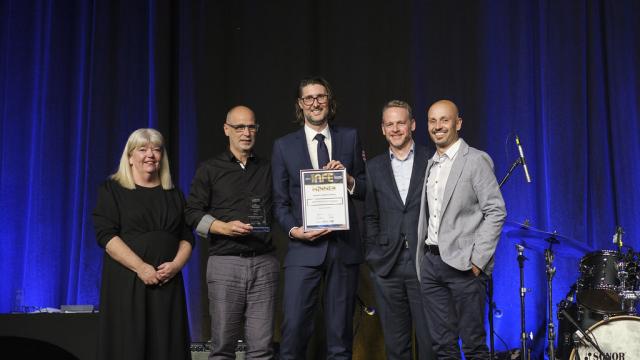 5 adults in evening dress stand on a stage holding a certificate