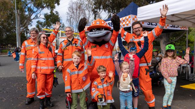a group of people waving. They are wearing SES uniforms. In the middle of the group is the SES platypus mascot.