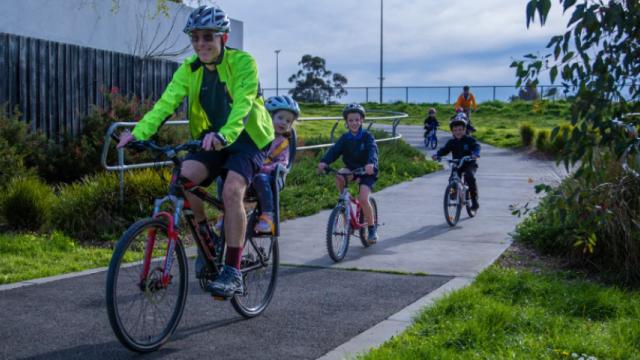 Smiling man rides bike on path followed by children on bikes