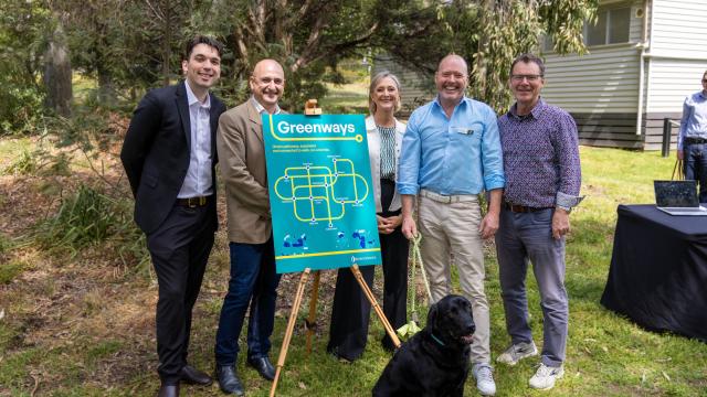 5 people and a dog stand before a Greenways poster