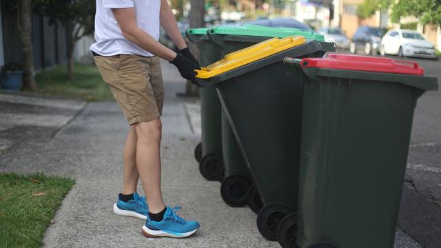 A man putting a recycling bin out on the kerb next to other bins