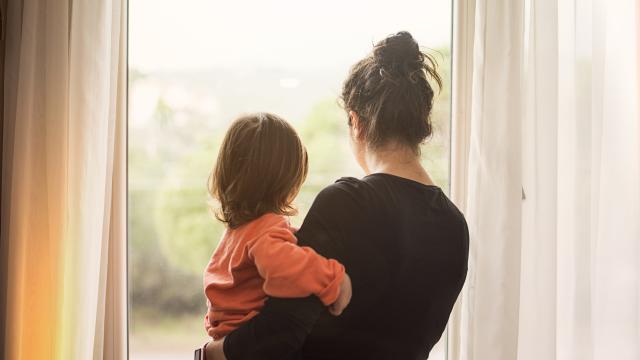 A woman holding a small child looks out the window.