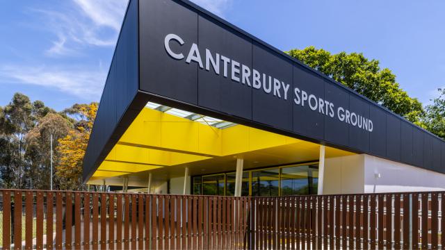 Black, yellow and white sports pavilion behind fence in park