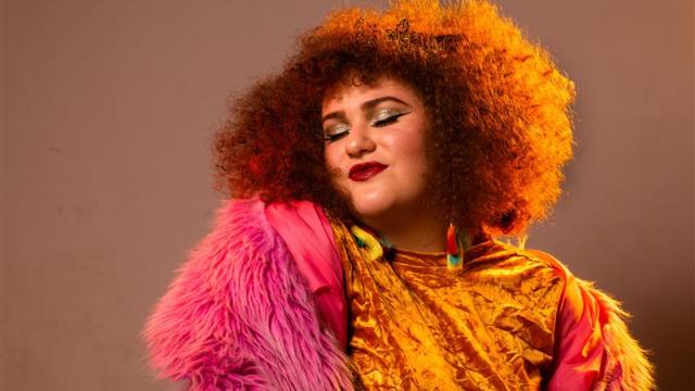 A drag queen with orange curly hair and a golden outfit