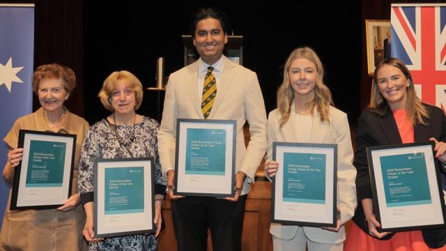 Five people holding citizen of the year awards standing together on a stage