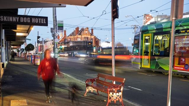Kew Junction streetscape with person walking dog and green and yellow tram passing by
