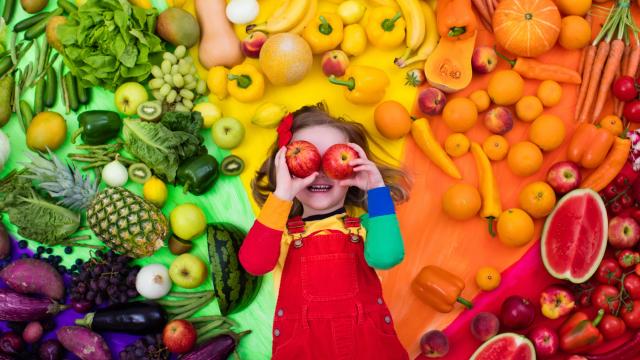 Young child is surrounded by rainbow of fruit and vegetables