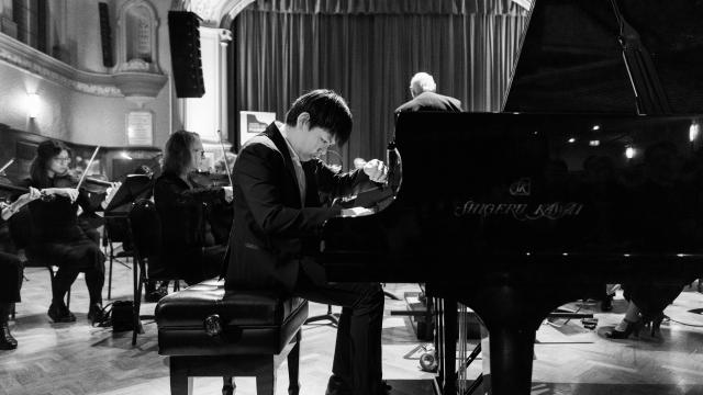 Teenage boy wearing suit plays grand piano