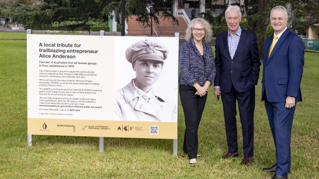 Commemorative plaque beside which 3 people in suits stand