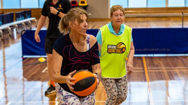 Player holds basketball on indoor basketball court with another player and referee in background