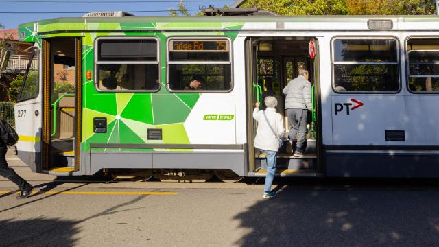 Two people climb into a green and white tram