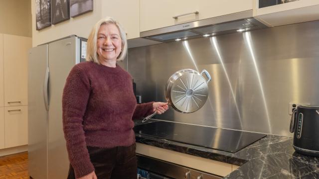 Woman in fluffy purple jumper holds shiny pan above black cooktop