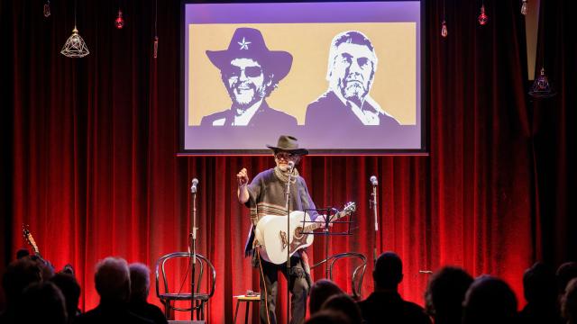 Guitarist wearing poncho and cowboy hat stands in front of audience
