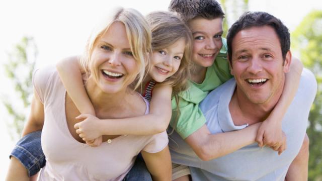 2 adults and 2 children smiling. The children are on the adults backs.