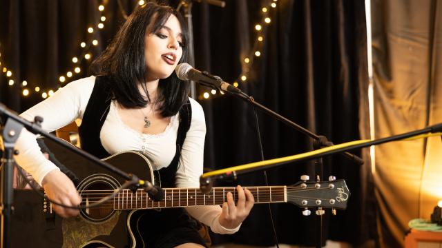 Young person playing guitar in front of a microphone.