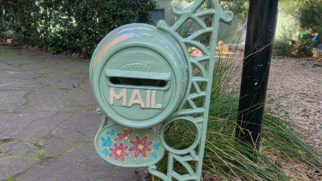 A round cast iron letterbox painted in pale green and painted with pink flowers.