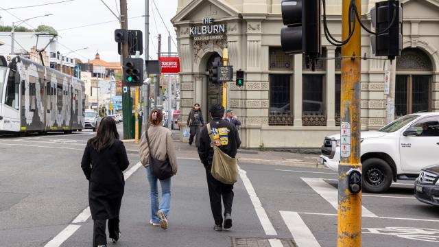 Several people cross a road at traffic lights with pub in background