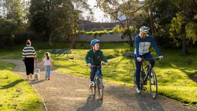 A dad and son cycle on a path while a mum and daughter walk their dog