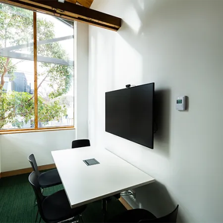 Study room with wall mounted screen, small desk and three chairs.