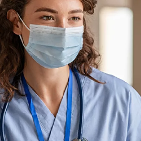 Female nurse wearing a face mask and talking to a patient who has their back to us.