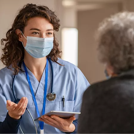 Nurse wearing a mask talking to a patient with their back to us.